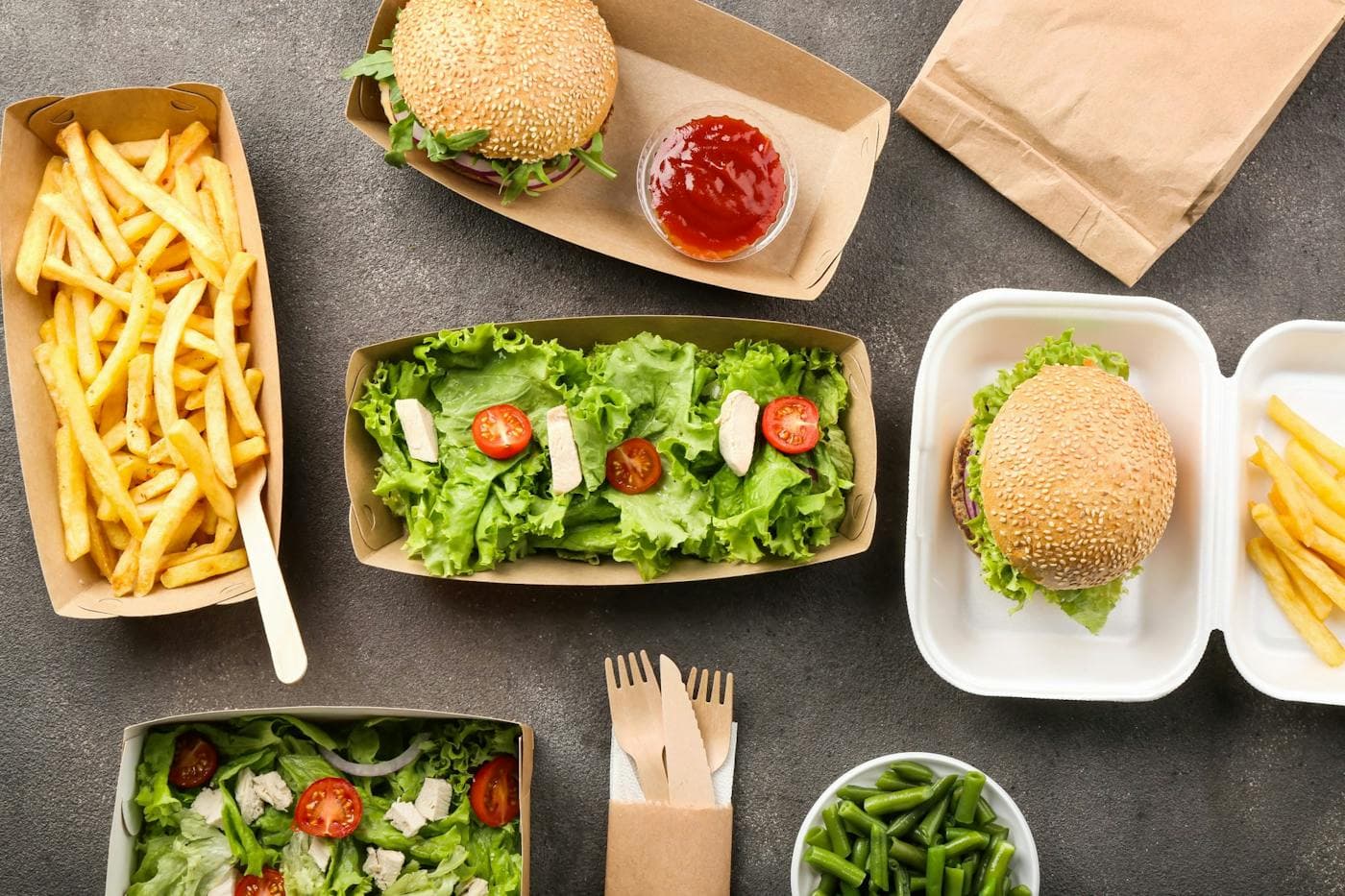 Burgers, fries and salad in takeaway boxes and trays